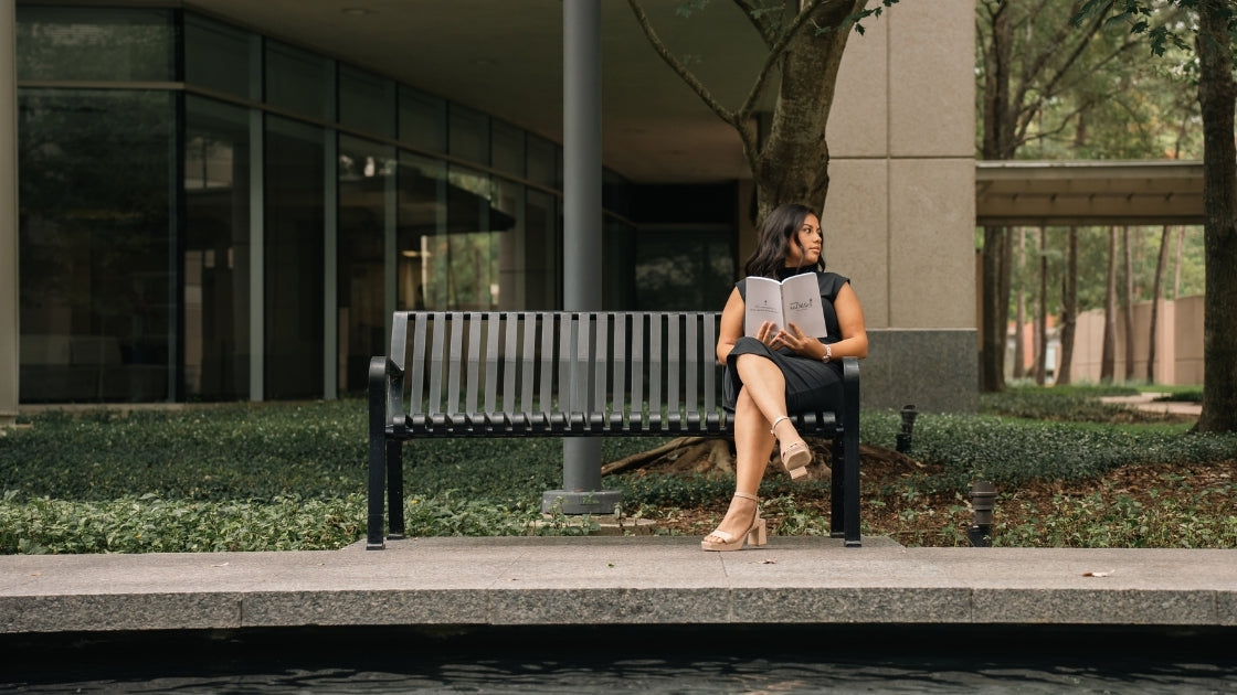 Woman reading a book on a bench outside a building